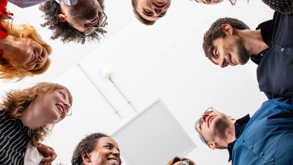 Directly below shot of smiling multi-ethnic male and female entrepreneurs huddling together in creative office