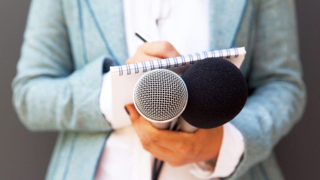 Female journalist at news conference, writing notes, holding microphone